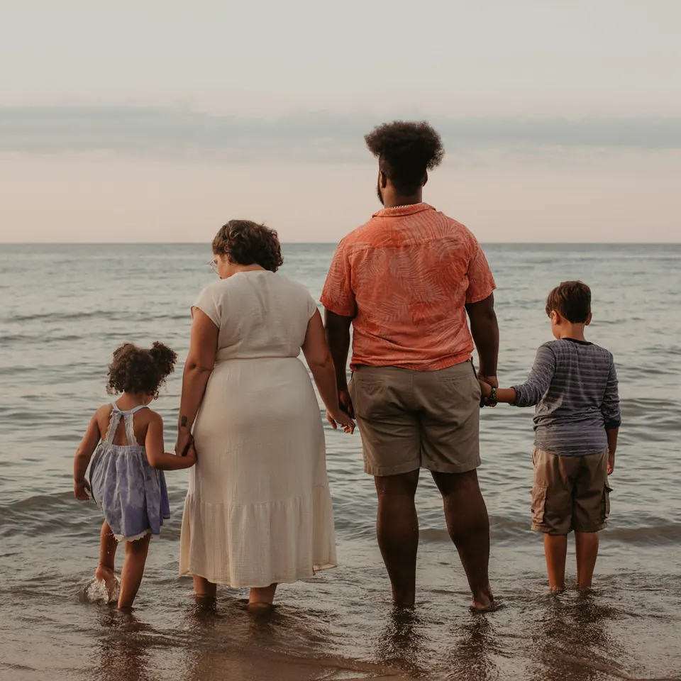 A family of four standing hand in hand at the edge of the sea